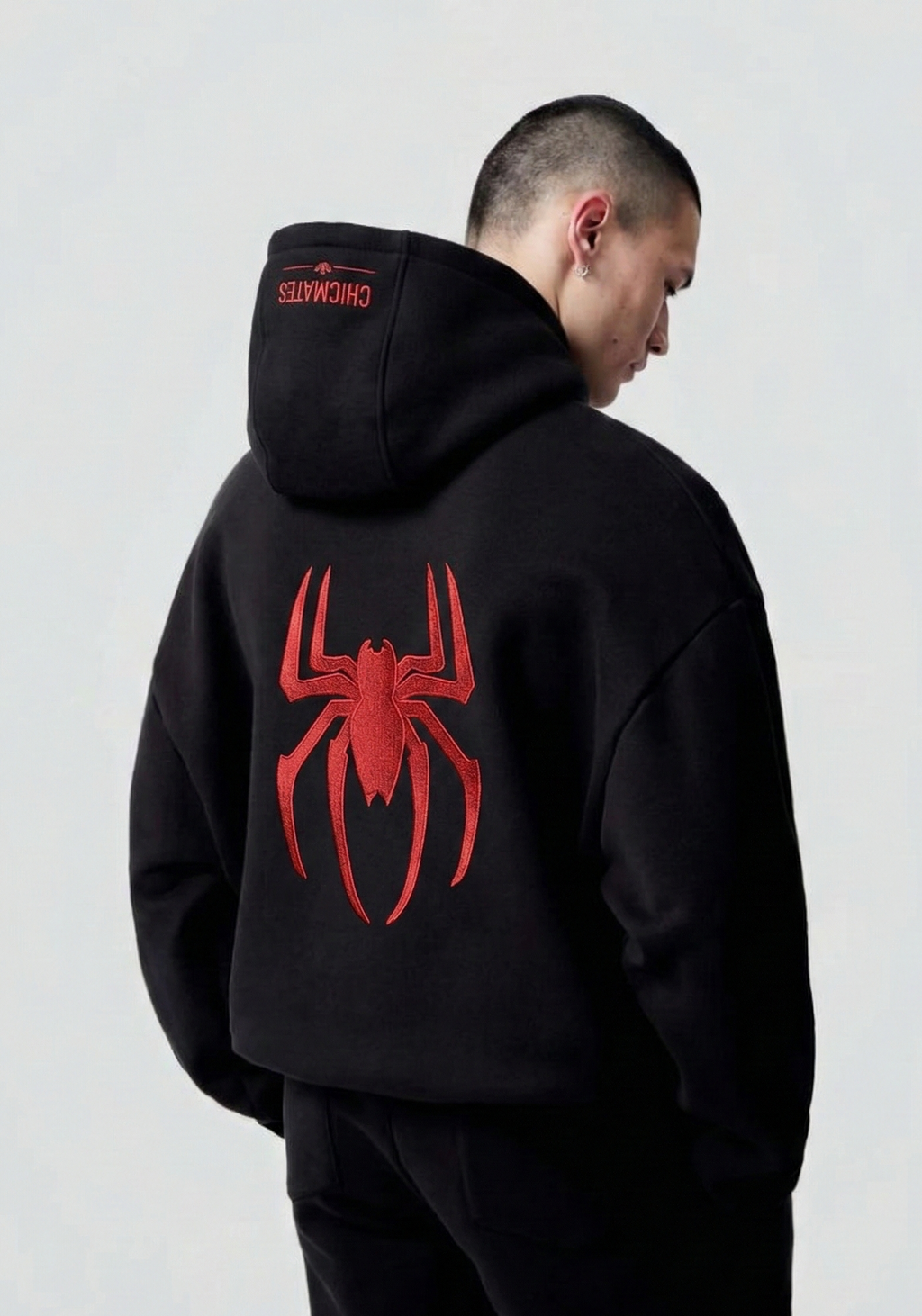 Person wearing a black hoodie with a red spider graphic on the back against a white background