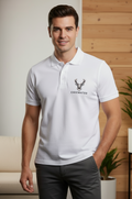 Man wearing a white polo shirt with a logo and text, standing in a room with wooden walls and plants.